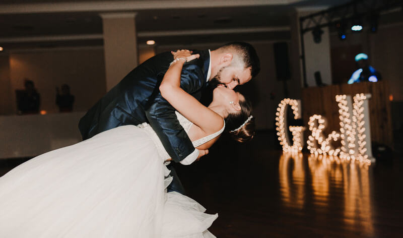 Bride and groom kissing with their initials illuminated in the background